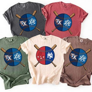 May include: Five short-sleeved t-shirts in various colors: charcoal, red, olive green, cream, and brown. Each shirt features a baseball design with crossed bats and team logos. The baseballs are split, with team names and logos on each side.