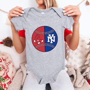 May include: A gray baby bodysuit featuring a baseball design. The baseball is split into red and blue halves, with a white sock graphic on the red side and the letters "NY" in white on the blue side. The bodysuit has short sleeves.