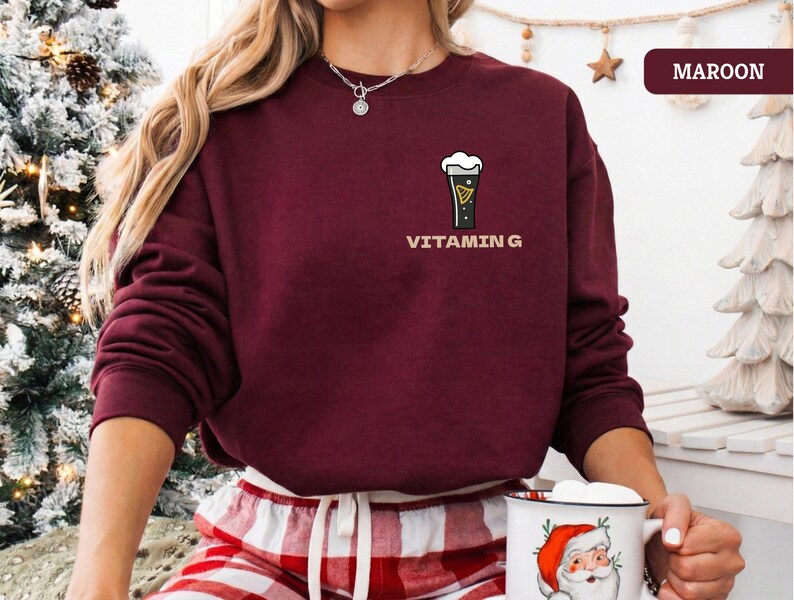 Puede incluir: Sudadera granate con un peque&ntilde;o gr&aacute;fico de una pinta de cerveza negra y la palabra "VITAMIN G" impresa debajo. La sudadera es de color granate liso y tiene mangas largas. La modelo lleva un pantal&oacute;n de pijama a cuadros rojos y blancos.