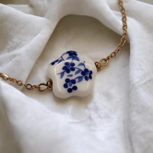 Gold-plated stainless steel bracelet with a ceramic flower bead and white and blue floral pattern. A trendy, minimalist, porcelain-effect gift for women.