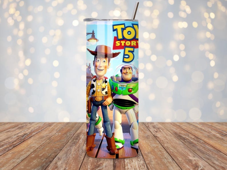 May include: A cylindrical stainless steel tumbler featuring a colorful graphic print of the characters Woody and Buzz Lightyear from the Toy Story franchise, with the text Toy Story 5 prominently displayed at the top and a metal straw inserted.
