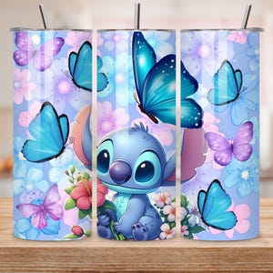May include: A cylindrical tumbler with a lid and straw featuring a light blue background decorated with various blue and purple butterflies and pink and white flowers. A blue cartoon character with large ears is centered holding a pink flower.