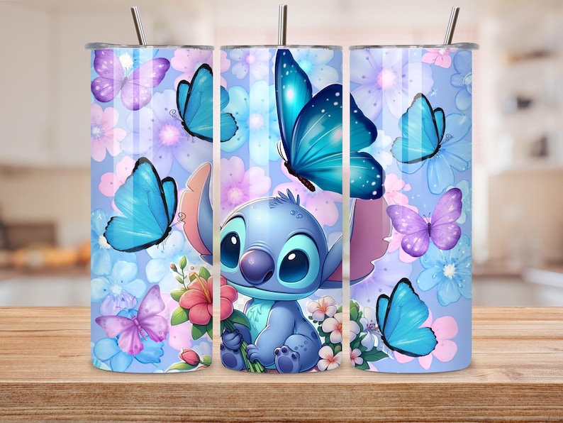 May include: A cylindrical tumbler with a lid and straw featuring a light blue background decorated with various blue and purple butterflies and pink and white flowers. A blue cartoon character with large ears is centered holding a pink flower.