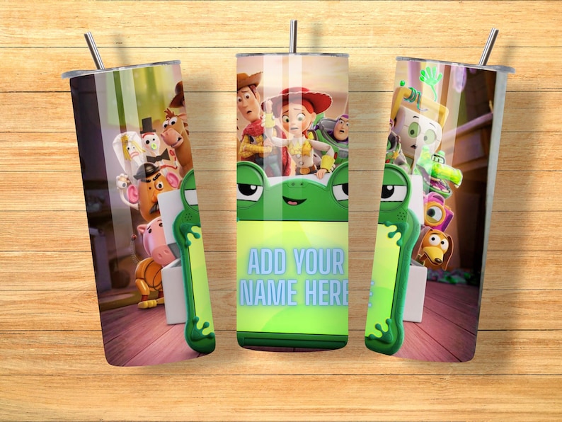 Op de afbeelding: Een cilindervormige metalen beker met een rondom lopende afbeelding van Toy Story-personages, waaronder Woody, Jessie en Buzz Lightyear. Het ontwerp bevat een groen kikker-vormig kader met de tekst ADD YOUR NAME HERE in lichtblauwe letters.