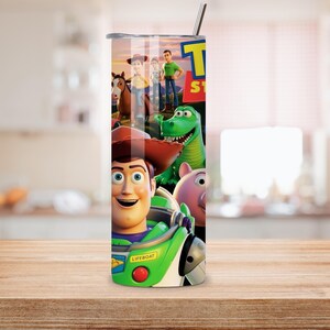 May include: A cylindrical stainless steel tumbler featuring a colorful graphic wrap of Toy Story characters including Woody, Buzz Lightyear, Rex, and Hamm. The design includes the Toy Story logo and a metal straw protruding from the top lid.