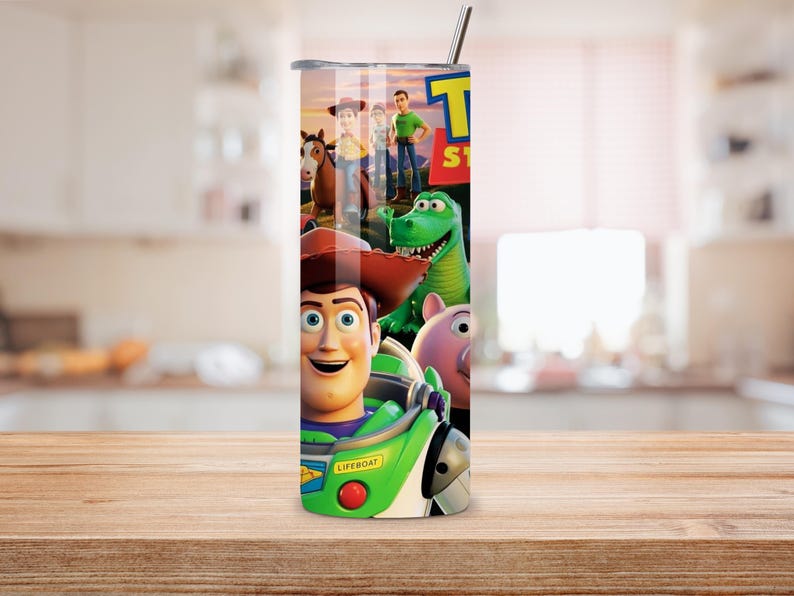 May include: A cylindrical stainless steel tumbler featuring a colorful graphic wrap of Toy Story characters including Woody, Buzz Lightyear, Rex, and Hamm. The design includes the Toy Story logo and a metal straw protruding from the top lid.