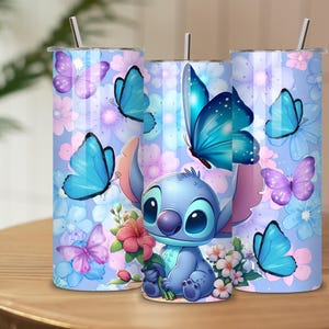 May include: Three cylindrical tumblers with metal straws featuring a light blue background, a cartoon character with large ears, blue and purple butterflies, and pink and white flowers. The design wraps around each tumbler with a consistent floral theme.