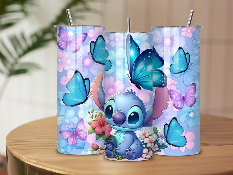May include: Three cylindrical tumblers with metal straws featuring a light blue background, a cartoon character with large ears, blue and purple butterflies, and pink and white flowers. The design wraps around each tumbler with a consistent floral theme.