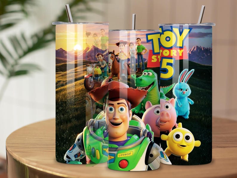 May include: Three cylindrical tumblers with metal straws featuring a Toy Story 5 graphic print. The design displays characters including Woody, Buzz Lightyear, Rex, Hamm, Ducky, and Bunny against a sunset landscape. The text Toy Story 5 is visible.