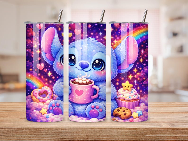May include: Three stainless steel tumblers with a cartoon character design. The design features a blue creature holding a pink mug with a heart, surrounded by sweets, rainbows, and stars. The tumblers have a silver lid and a straw.