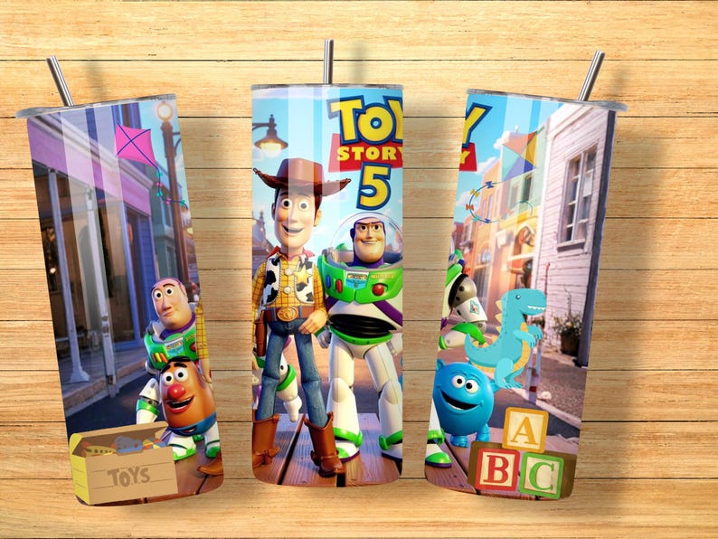May include: A cylindrical tumbler featuring a Toy Story 5 graphic with Woody, Buzz Lightyear, Rex, and Mr. Potato Head. The design includes a toy box labeled TOYS, alphabet blocks, and a street scene background. A metal straw is inserted at the top.