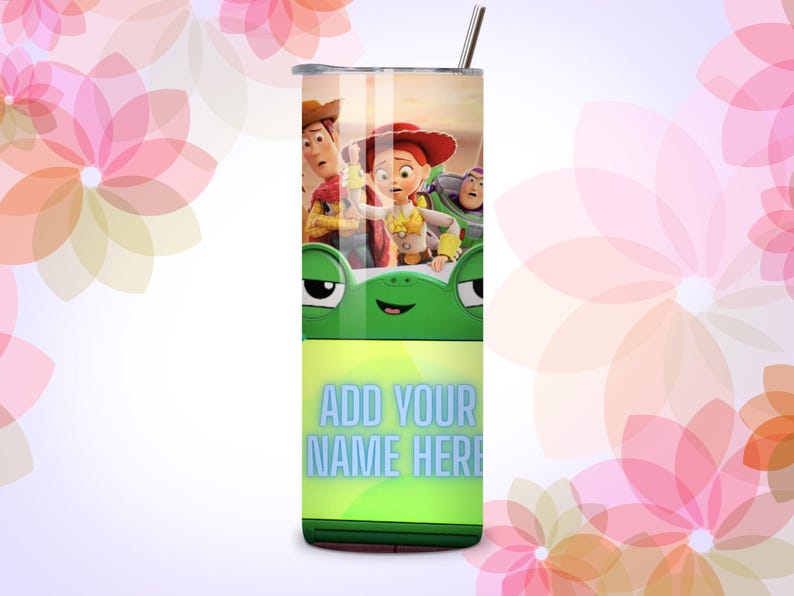 Op de afbeelding: Een cilindervormige metalen beker met rietje, voorzien van een Toy Story-personageafbeelding aan de bovenkant, een groen kikkergezicht in het midden en de tekst ADD YOUR NAME HERE in lichtblauwe letters op een limoengroene achtergrond.