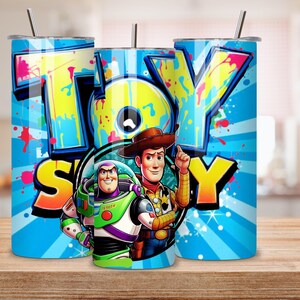 K&ouml;nnte beinhalten: Ein Set aus drei Edelstahlbechern mit Deckeln und Strohhalmen. Jeder Becher hat ein lebendiges Design mit dem Wort "TOY STORY" im Graffiti-Stil sowie Bildern von Woody und Buzz Lightyear vor einem blauen Hintergrund mit radialen Linien und Farbspritzern.