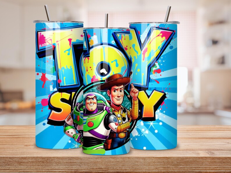 K&ouml;nnte beinhalten: Ein Set aus drei Edelstahlbechern mit Deckeln und Strohhalmen. Jeder Becher hat ein lebendiges Design mit dem Wort "TOY STORY" im Graffiti-Stil sowie Bildern von Woody und Buzz Lightyear vor einem blauen Hintergrund mit radialen Linien und Farbspritzern.