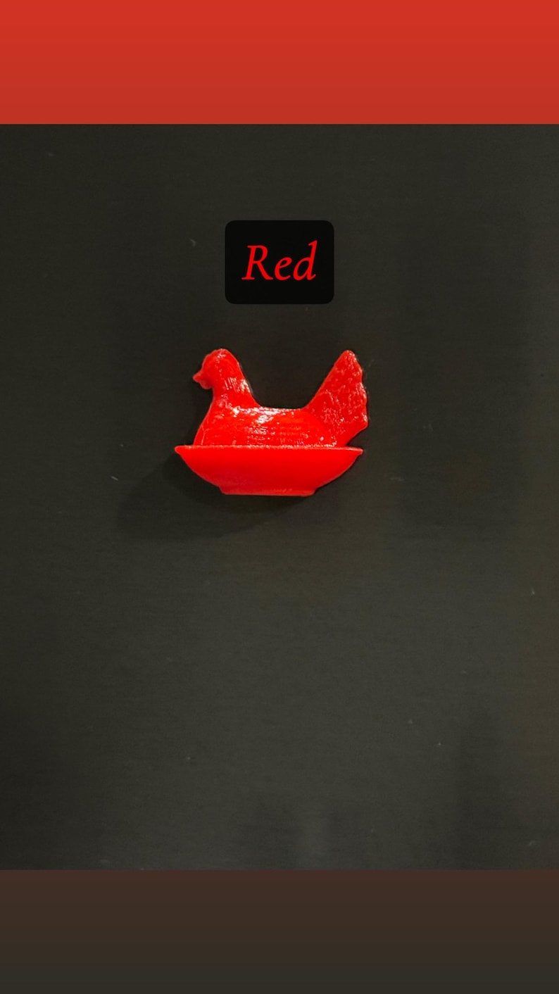 May include: A bright red hen figurine sitting in a red bowl. The word "Red" is displayed in a black box above the figurine. The background is a solid black.