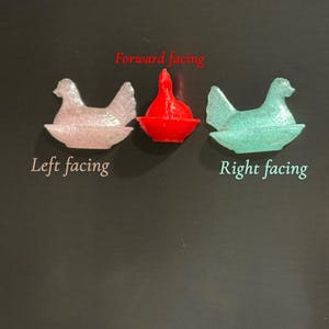 May include: Three small, decorative hen figurines in pink, red, and teal. The text "Forward facing", "Left facing", and "Right facing" are above and below the hens. The hens are on a dark surface.