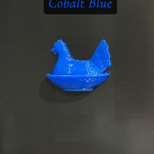 May include: A cobalt blue hen figurine in a nest. The text "Cobalt Blue" is displayed in a black rectangle above the figurine. The hen is a solid color and appears to be 3D printed.
