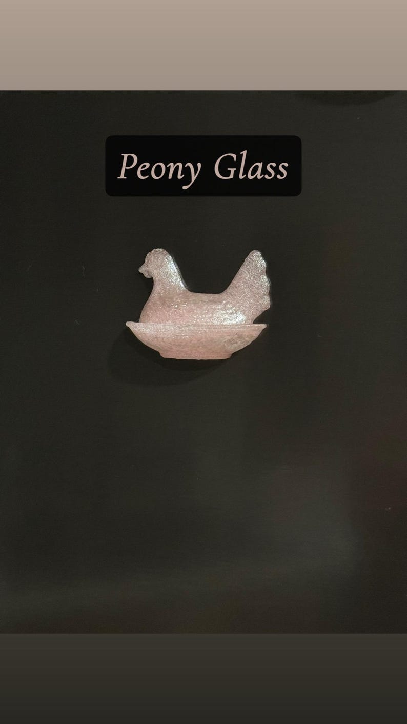 May include: A pink glass hen figurine in a nest shape. The figurine is made of textured glass and sits on a dark background. The text "Peony Glass" is displayed above the figurine.