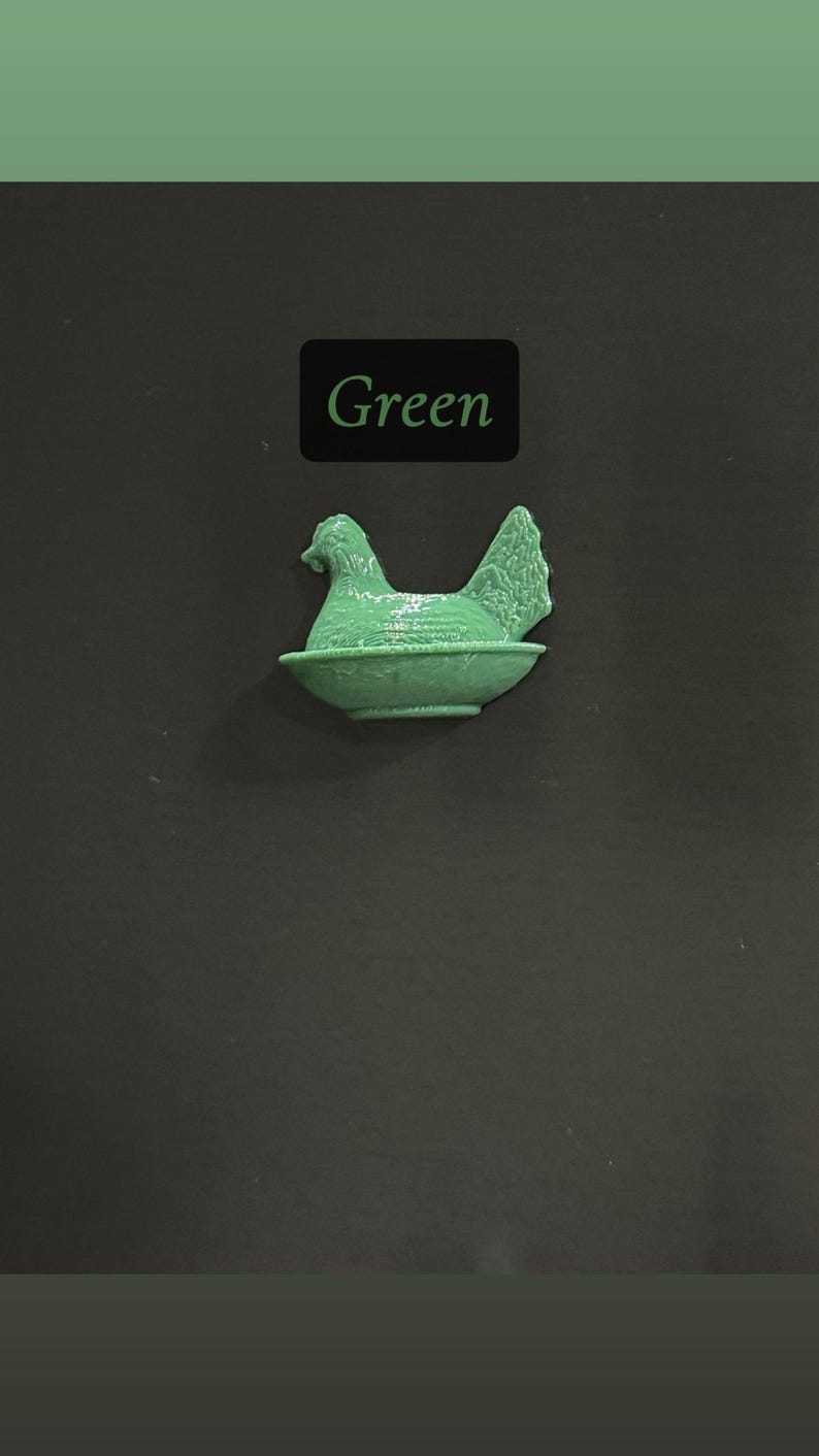May include: A green hen figurine in a nest-like bowl. The word "Green" is displayed in a black rectangle above the figurine. The background is a dark gray color.