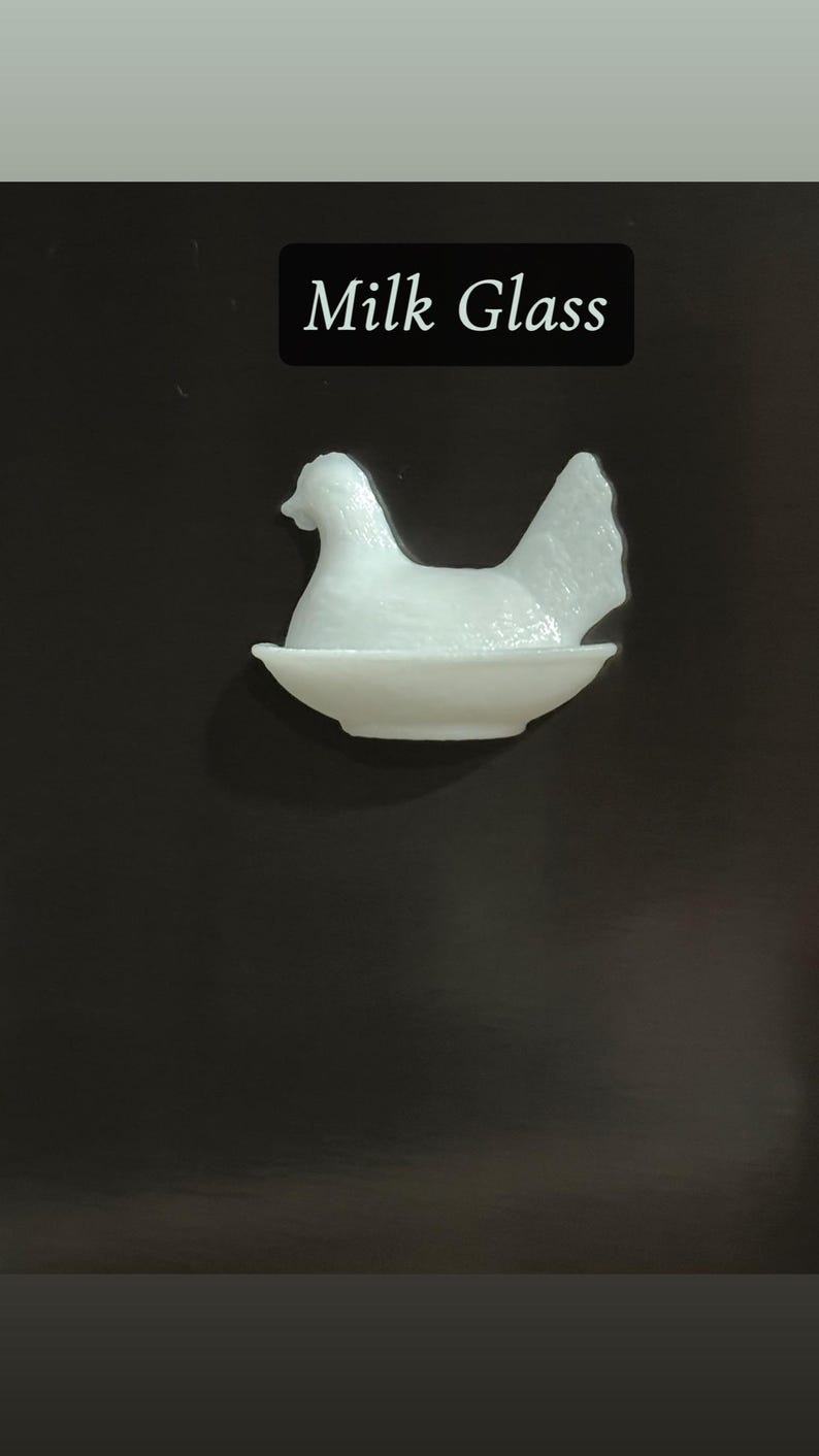 May include: A white milk glass hen figurine sitting in a shallow dish. The hen is detailed with a textured surface and is set against a dark background. The text "Milk Glass" is displayed in a black rectangle.