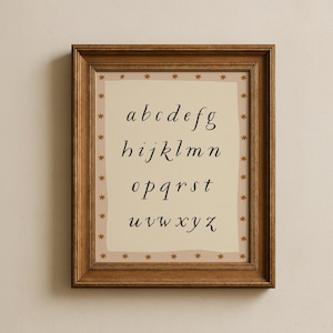 May include: A framed print featuring the lowercase alphabet in a cursive font. The letters are black on a cream-colored background. The frame is a dark brown wood, and the print is bordered with small gold stars.