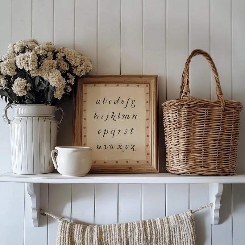 May include: A decorative shelf displays a framed alphabet print, a woven basket, a ceramic vase with flowers, and a small mug. The alphabet print is in a wooden frame with star accents. The vase and mug are cream-colored.
