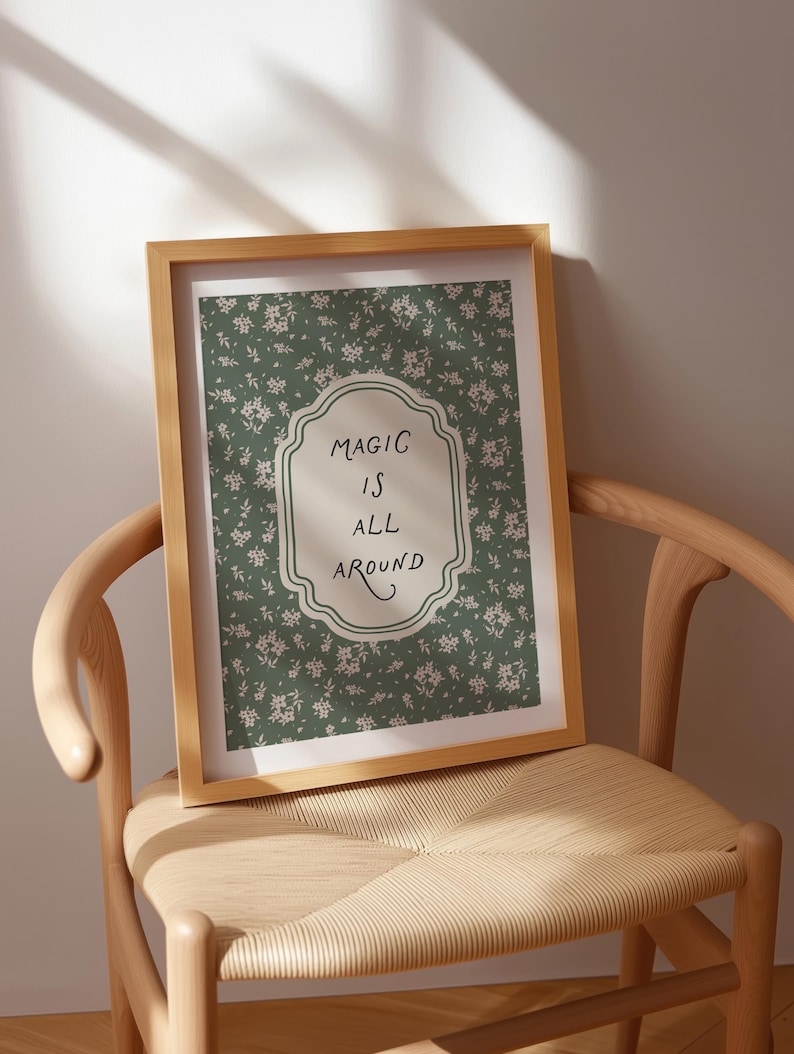 K&ouml;nnte beinhalten: Ein gerahmter Druck mit den Worten "MAGIC IS ALL AROUND" in einem dekorativen Rahmen. Der Druck hat einen gr&uuml;nen floralen Hintergrund. Der Rahmen besteht aus hellbraunem Holz, und der Druck wird auf einem Holzstuhl pr&auml;sentiert.