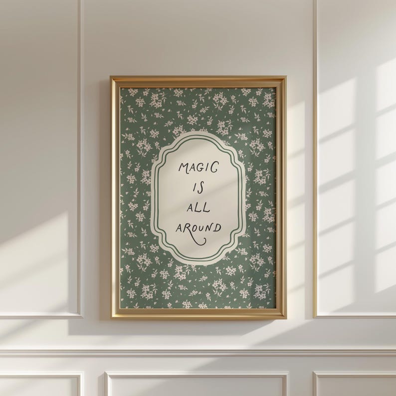 K&ouml;nnte beinhalten: Ein gerahmter Druck mit einem goldfarbenen Rahmen. Der Druck zeigt einen gr&uuml;nen floralen Hintergrund und eine cremefarbene zentrale Form mit den Worten "MAGIC IS ALL AROUND" in schwarzer Schrift. Der Druck ist an einer wei&szlig;en Wand befestigt.