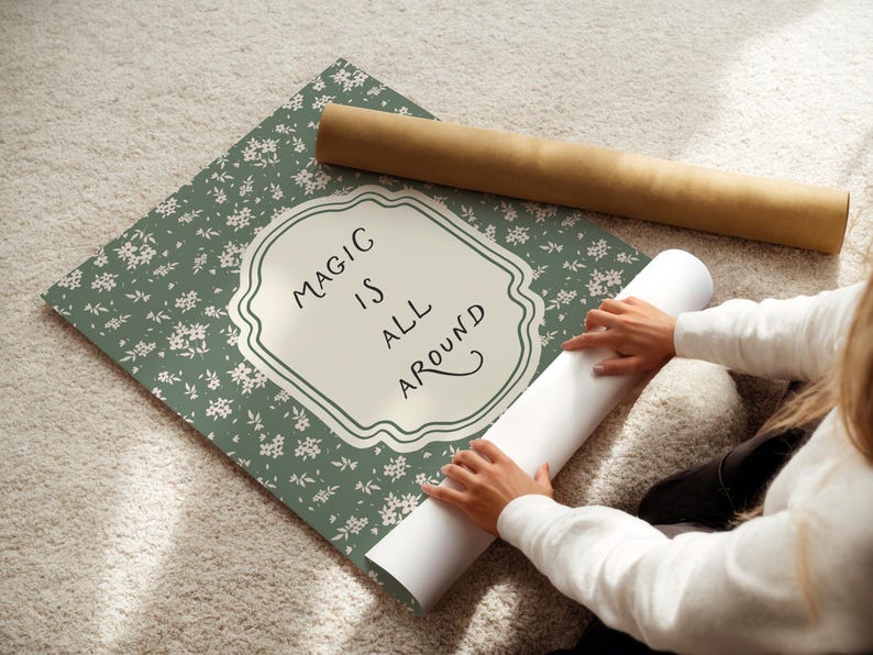 K&ouml;nnte beinhalten: Ein Poster mit floralem Muster und dem Schriftzug "MAGIC IS ALL AROUND" in einem dekorativen Rahmen. Ein aufgerolltes Poster und eine braune Rolle sind ebenfalls zu sehen.