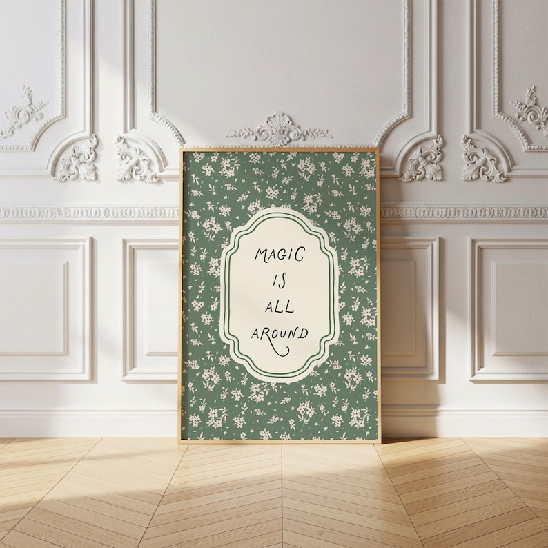 K&ouml;nnte beinhalten: Ein gerahmter Kunstdruck mit einem goldenen Rahmen. Der Druck zeigt einen gr&uuml;nen floralen Hintergrund mit einem cremefarbenen, verzierten Mittelteil. In der Mitte steht der Schriftzug "MAGIC IS ALL AROUND" in schwarzer Schrift.