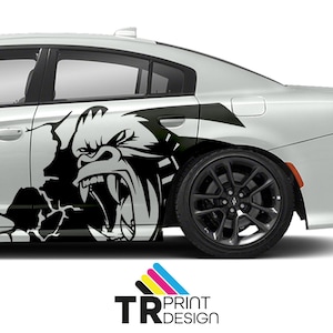 May include: A white car with a black and white gorilla graphic on the side. The gorilla is roaring, with its teeth bared. The graphic appears to be breaking through the car's surface. The car has black rims and a spoiler.