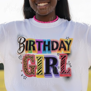 May include: White t-shirt with the words "BIRTHDAY GIRL" in colorful, block letters. The word "BIRTHDAY" is in a script font with a black outline. The letter "G" in "GIRL" has a leopard print design.