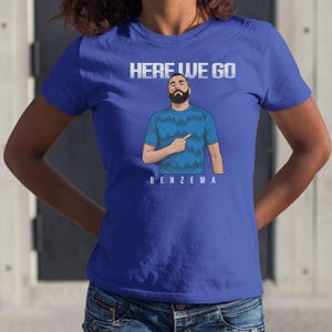 A person wearing a blue t-shirt with a graphic of a bearded man and the text "HERE WE GO BENZEMA" printed on it.