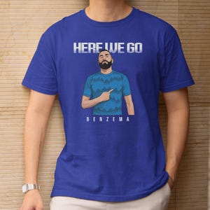 A blue t-shirt with a graphic design depicting a man with a beard and the text "HERE WE GO BENZEMA" printed on it.