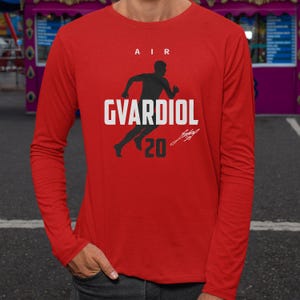 A person wearing a red long-sleeved shirt with a graphic design featuring a silhouette of a person running and the text "AIR GVARDIOL 20" printed on it.