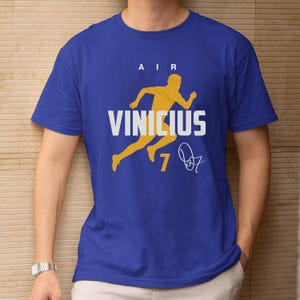 A blue t-shirt with a yellow silhouette of a person running and the text "AIR VINICius 7" printed on it.