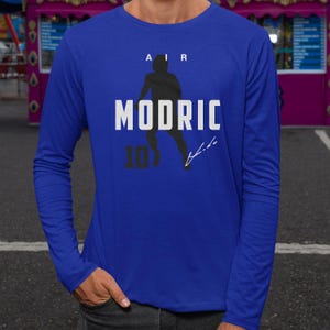 A person wearing a blue long-sleeved shirt with a graphic design featuring a silhouette of a person and the text "MODRIC 10" printed on it.