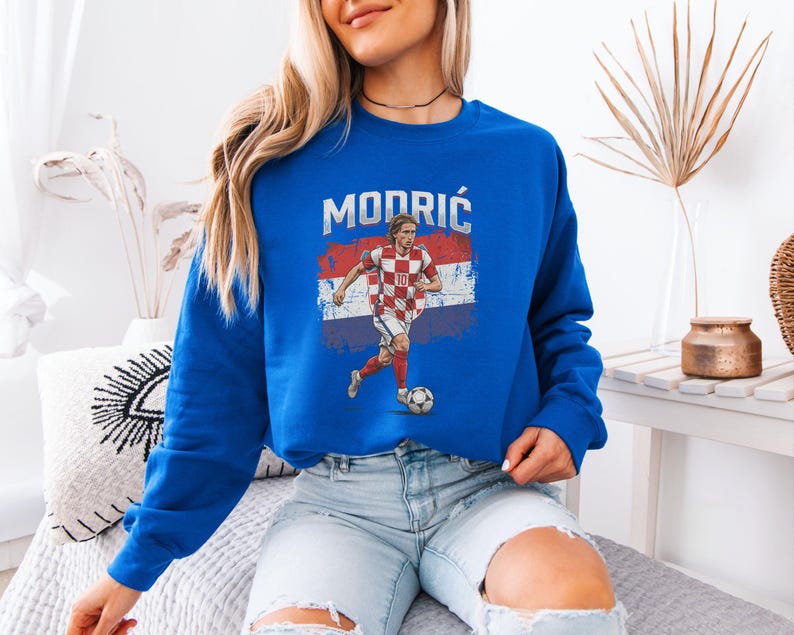 A woman wearing a blue sweatshirt with a graphic of a soccer player and the word "MODRIC" printed on it.