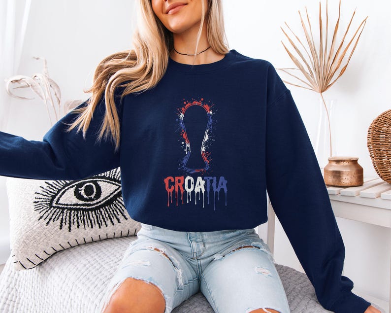 A woman wearing a navy blue sweatshirt with a graphic of the European Cup and the word "CRCATIA" printed on it, sitting on a couch.