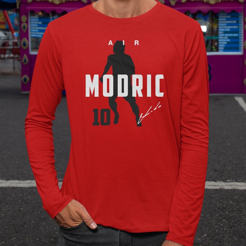 A man wearing a red long-sleeved shirt with a graphic design featuring a silhouette of a person and the text "MODRIC 10" printed on it.