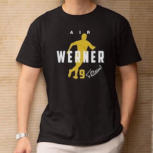 May include: Black t-shirt featuring a yellow silhouette of a soccer player with the name "WERNER" in white. The number "9" and a signature are also in yellow. The word "AIR" is above the player.