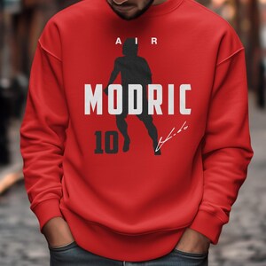 A man wearing a red sweatshirt with the text "AIR MODRIC 10" printed on it.