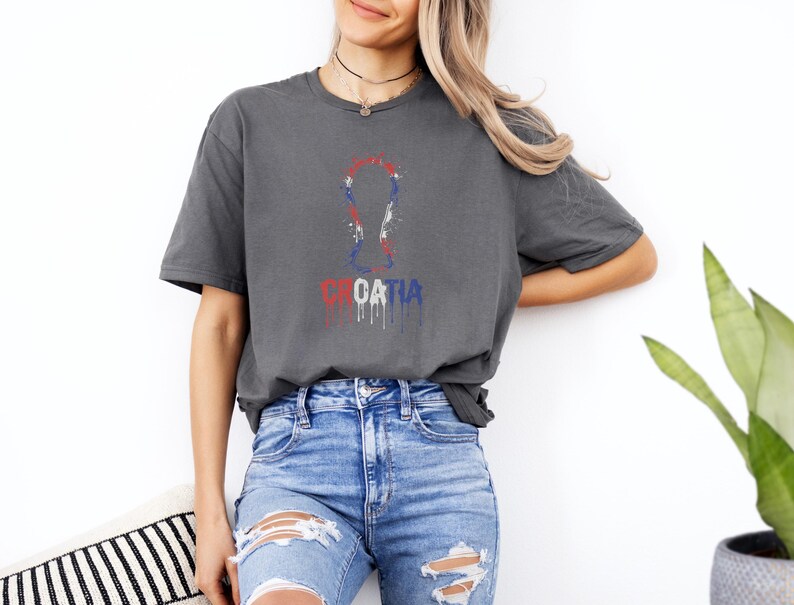 A woman wearing a gray t-shirt with a graphic of the European Cup and the word "Croatia" printed on it, standing against a white wall.