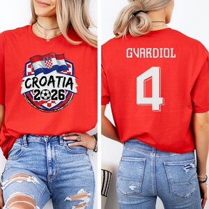 A woman wearing a red t-shirt with a graphic of the Croatia national flag and the text "Croatia 2026" printed on it.