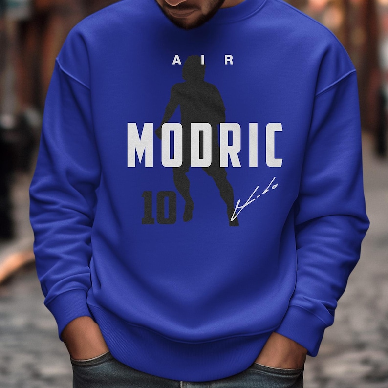 A man wearing a blue sweatshirt with a graphic design featuring a silhouette of a person and the text "MODRIC 10" printed on it.
