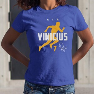 A woman wearing a blue t-shirt with a graphic design featuring a yellow figure and the text "AIR VINICUS 7".