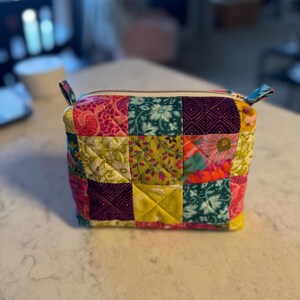 Peut inclure: Petite trousse zipp&eacute;e en patchwork aux motifs floraux et g&eacute;om&eacute;triques multicolores : rose, vert, jaune et violet. Le sac rectangulaire est orn&eacute; de petites boucles en tissu &agrave; chaque extr&eacute;mit&eacute; et d'une fermeture &eacute;clair.