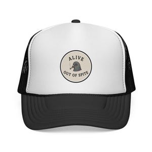 May include: Black and white trucker hat with a curved brim. The hat features a white front panel with a circular patch that reads "ALIVE OUT OF SPITE" around a smoking pigeon illustration. The mesh back is black.