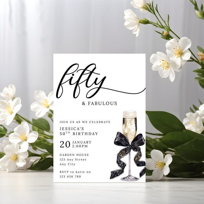 May include: A white invitation card with the words "Fifty & Fabulous" in elegant black script. The card includes details for Jessica's 50th birthday, a champagne glass illustration, and a black ribbon. White flowers frame the invitation.