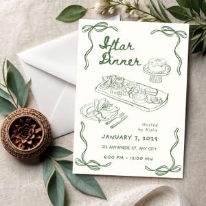 May include: An invitation card with the text "Iftar Dinner" in green script, featuring illustrations of food and a cake. The card includes the date, time, and location, with decorative green bows. A white envelope and a woven basket are also visible.